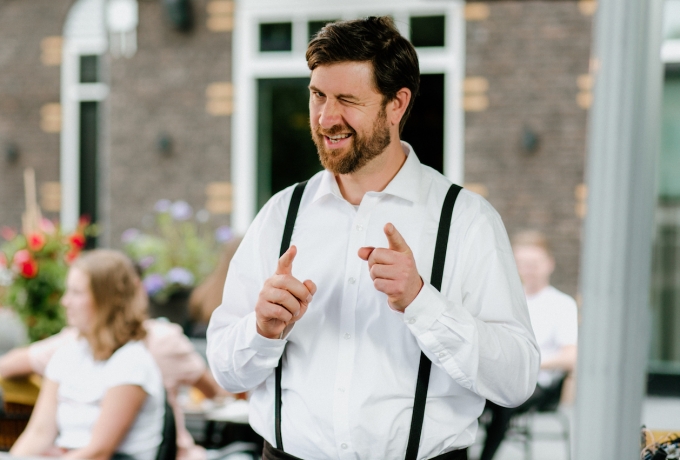 Horecamedewerker Pepijn staat op terras lacht en knipoogt omdat hij slim bezig door Apprendo.